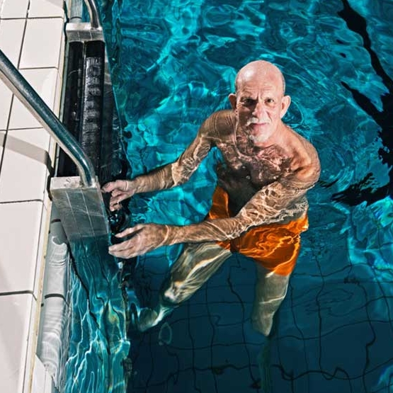 älterer Mann an Leiter im Schwimmbad