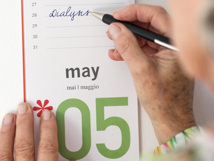 Eine Hand schreibt die Dialyse für 28. Mai mit einem Kugelschreiber in einen Kalender