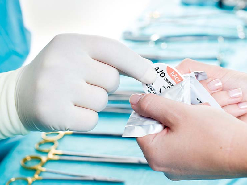 La main gantée retire le matériel de suture d’un emballage stérile