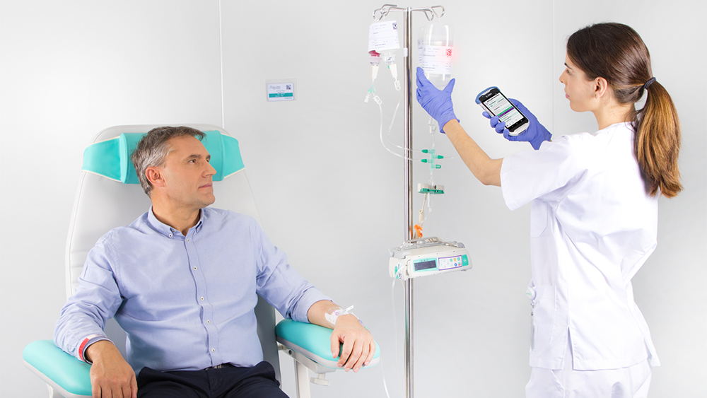 L’image montre un patient assis dans un fauteuil recevant une perfusion d’un dispositif médical B. Braun, tandis qu’une infirmière configure le dosage de la perfusion sur le dispositif.