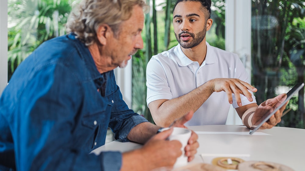 Un homme d’âge moyen et un médecin sont assis à une table et interagissent avec une tablette