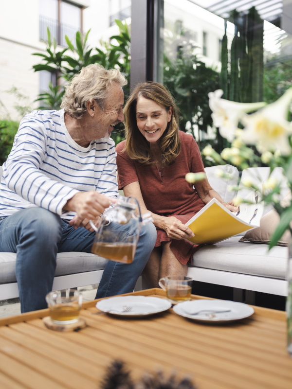 Un homme avec une théière et une femme avec un magazine assis sur un canapé et riant
